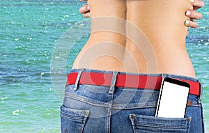 Smartphone with white screen with empty space for text in a jeans pocket of a young slender girl, ocean background