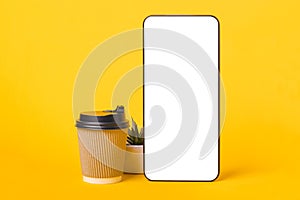 Smartphone with white screen and paper coffee cup on yellow background copy space