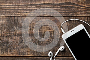 Smartphone. White telephone with headphones on a brown wooden table. view from above