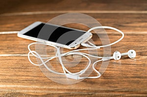 Smart cell phone with white wired headphones on a wooden board photo