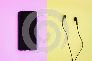 Smartphone and Wired earphones on pink and yellow background
