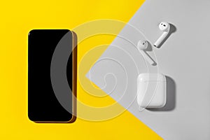 Smartphone and wireless headphones on yellow and gray background.