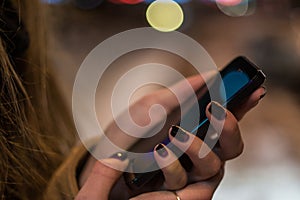 Smartphone in woman hands in front of blurred city lights