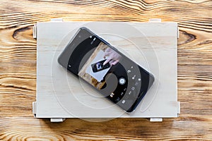 Smartphone on a wooden box with itself image on screen. Remote camera control application concept