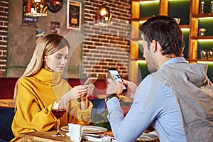 Always with smartphone. Young couple are sitting in restaurant with smartphones