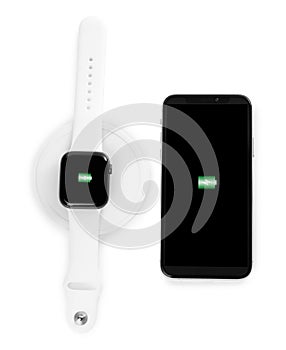 Smartwatch charging with wireless pad and mobile phone isolated on white