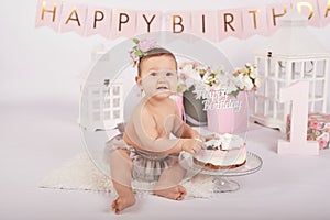 Smash cake party. Little cheerful birthday girl with first cake. Happy infant baby celebrating his first birthday. Decoration and