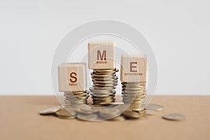 SME Startup Idea ,wooden cube blocks with SME abbreviations of Small and Medium Enterprises, on stack of coins