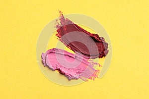 Smears of bright lipsticks on yellow background, top view