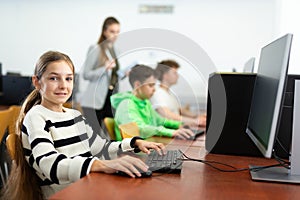 Smiilng teen schoolgirl sitting at table in computer class