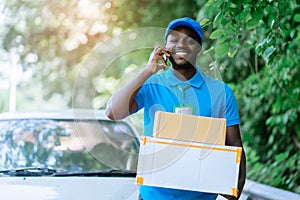 Smile african postal delivery courier man in front of car delivering package with talking smartphone