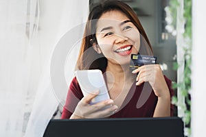 Smile Asian girl happy shopping online from home hand holding credit card and smart phone