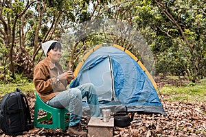 Smile asian young man hold cup of  coffee out the tent. drinking coffee in forest, alone lifestyle vacation camping