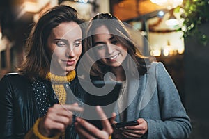 Smile bloggers together point finger on screen smartphone on night light city, hipsters friends using in hands mobile phone