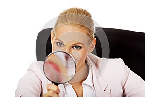 Smile business woman sitting behind the desk and looking into a magnifying glass