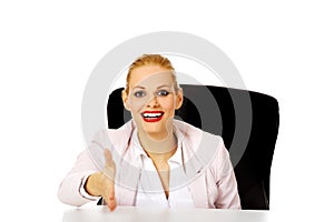 Smile business woman sitting behind the desk with an open hand ready for handshake