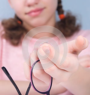 smile, close-up, hand holds eye glasses, and there is a lens on a finger to improve vision