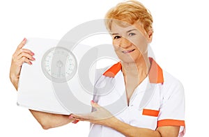 Smile elderly female doctor or nurse holds weigh scale