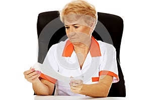 Smile elderly female doctor or nurse sitting behind the desk and holds bandage