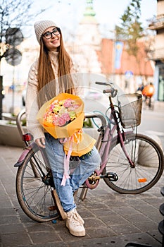 Smile on a face of a girl in hat stands near a bicycle on a city street