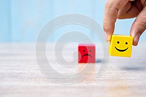Smile face on yellow wood cube and sad face icon on red wood cube. Service rating, ranking, customer review, satisfaction and