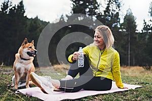 Smile girl  with shiba inu dog together relax after exercising outdoors on yoga mat, pet on nature with fitness woman drink water