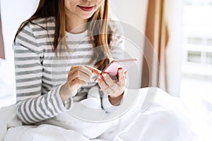 Smile happy young asian woman relaxing and using smart phone on the bed