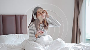 Smile happy young woman relaxing and using headphones to listen to music from smart phone in bedroom