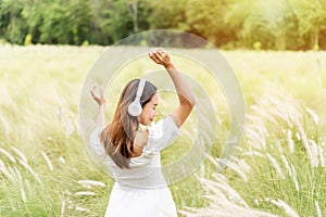 Smile happy young woman relaxing and using headphones to listen to music from smart phone in the flower field