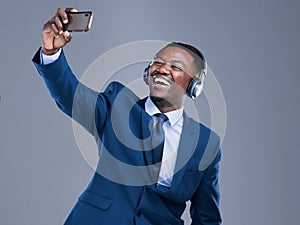Smile Its selfie time. Studio shot of a handsome young businessman using his cellphone to take selfies while listening