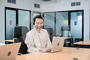 Smile operator asian gay agent with headset working with laptop on customer consultation in the office at call centre