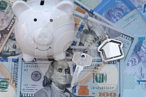 Smile piggy bank with home key chain on US dollar background. Saving for property investment concept