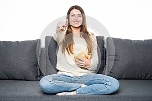 Smile and pointed Young woman watching TV and eating chips on sofa