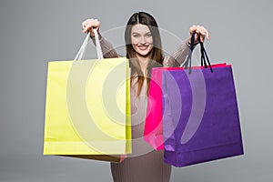 Smile shopper wearing dress showing blank colorful shopping bags and pointing you on grey background