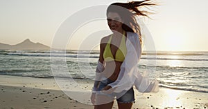 Smile, sunset and woman walking at the beach on holiday, vacation or travel in summer lens flare. Portrait of happy