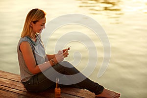 Smile woman sitting on dock and looking at celphone