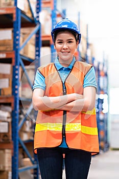 Smile woman worker crossed arm and standing in the warehouse distribution center. Engineer wears a safety helmet and vest. In