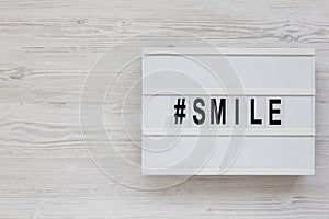 `Smile` word on a lightbox on a white wooden background, top view. Flat lay, from above, overhead. Space for text