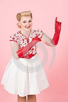Smiled and happy blonde girl sales space on pink background. Blonde girl pointing by fingers up. Lady with red gloves on hands poi