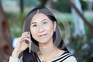 A smiley Asian girl cheerfully talking on the phone looking dir