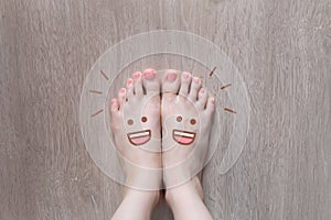 Smiley Face Drawn on Toes. Close Up Female Barefoot On Wooden Floor Background