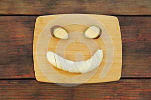 Smiley face made with banana slices on wooden table, top view