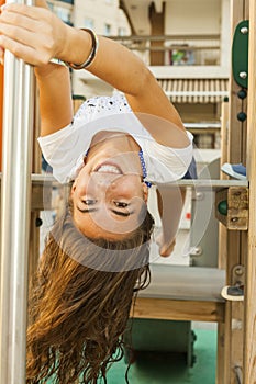 Smiley girl with long hair upsidedown in a swing at the park in