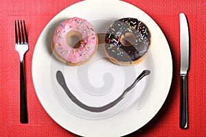 Smiley happy face made on dish with donuts eyes and chocolate syrup as smile in sugar and sweet addiction nutrition