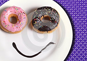 Smiley happy face made on dish with donuts eyes and chocolate syrup as smile in sugar and sweet addiction nutrition