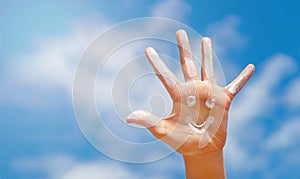 The smiley positive symbol drawing by sunscreen sun cream, suntan lotion on the caucasian open hand on blue sky.