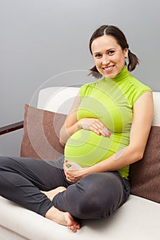 Smiley pregnant woman sitting on sofa