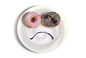 Smiley sad face made on dish with donuts as eyes and chocolate syrup mouth in sugar sweet addiction diet and nutrition