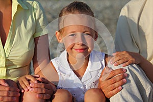 Smiliing daughter sitting between parents on beach