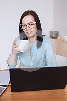 Smiliing woman drinking coffee while working online from home